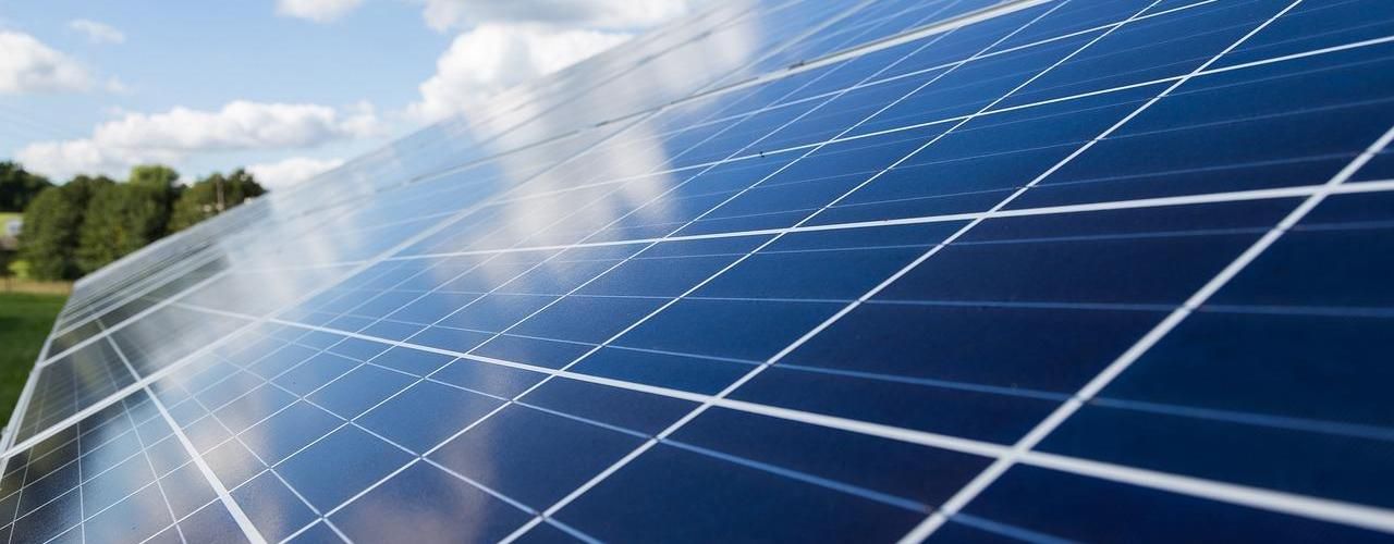 A solar panel with the sky above, clouds reflected on the shiny surface